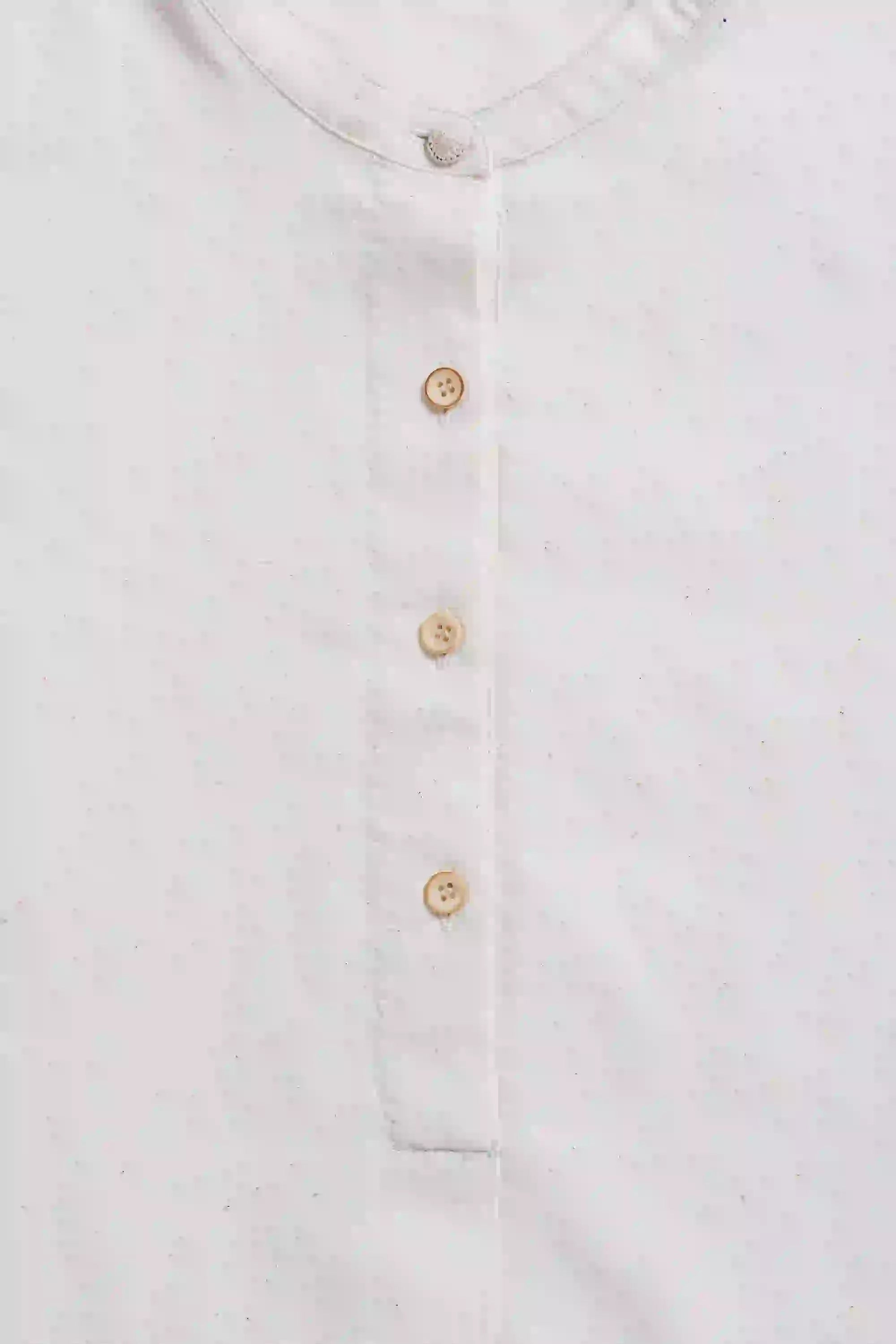 Close-up of a white shirt with gold buttons on a light gray background