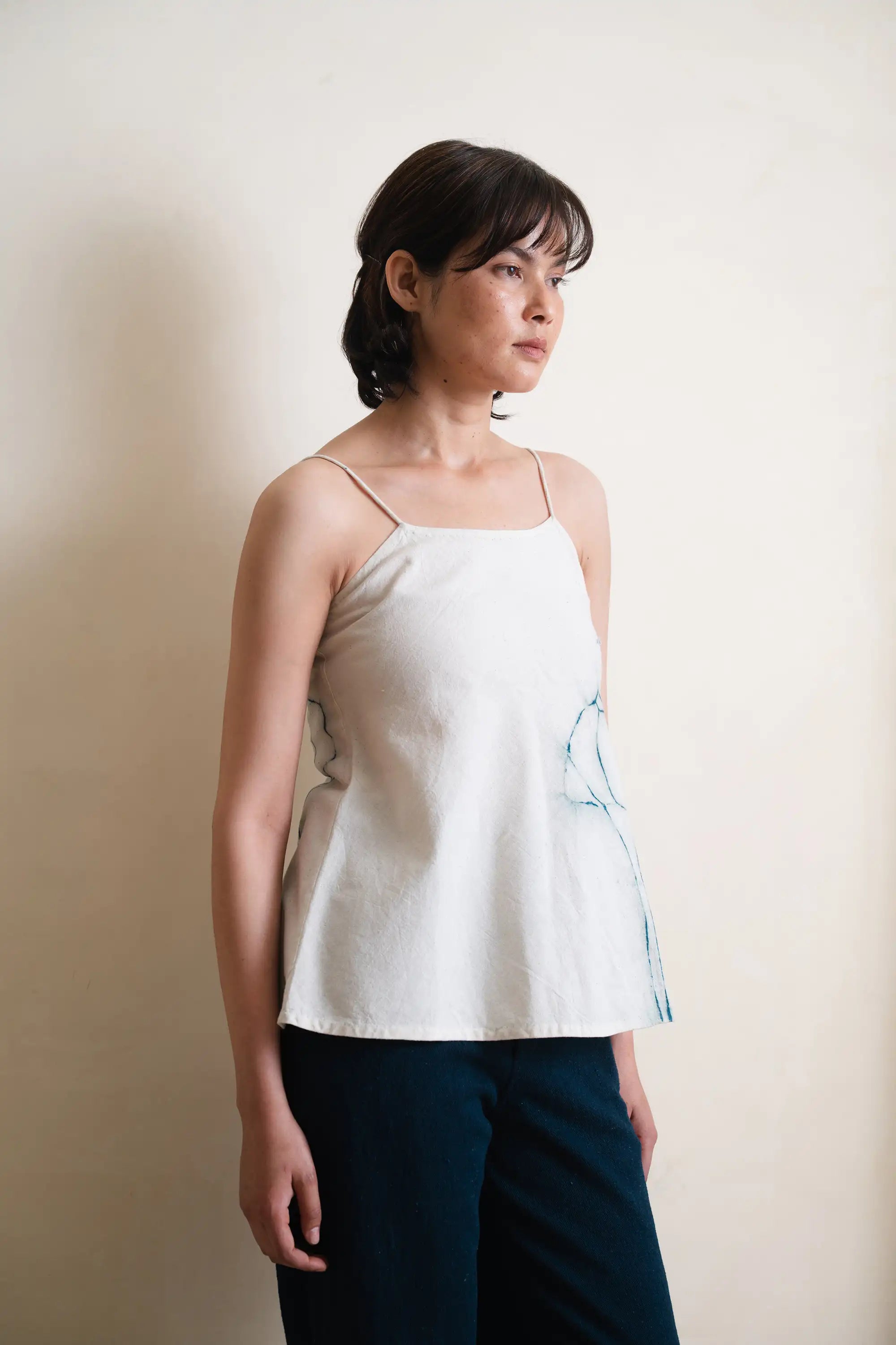 Woman wearing a light-colored tank top with a subtle design against a plain background