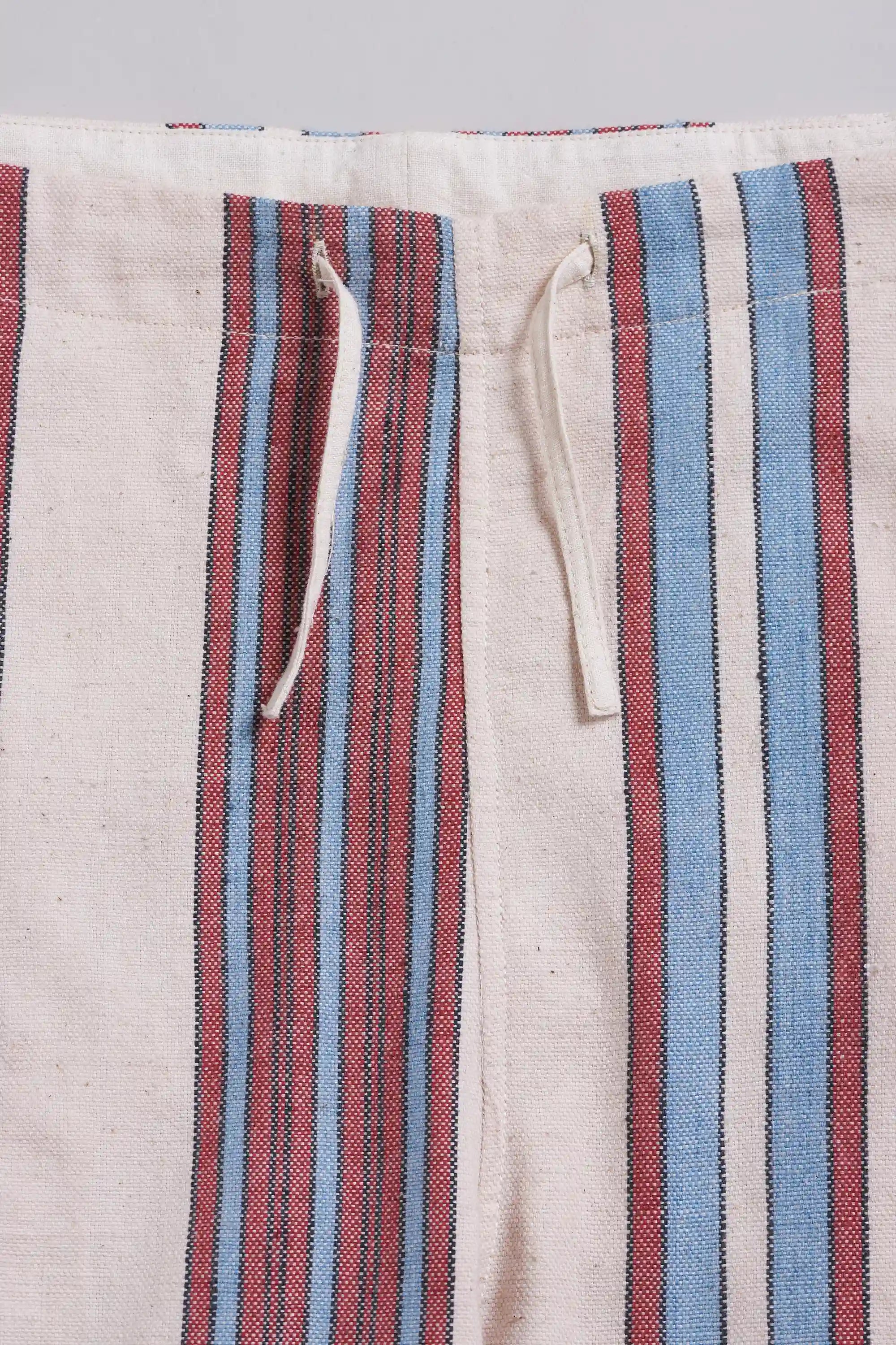 Close-up of striped fabric with vertical red, blue, and off-white stripes, plus a cream drawstring at the waistband.