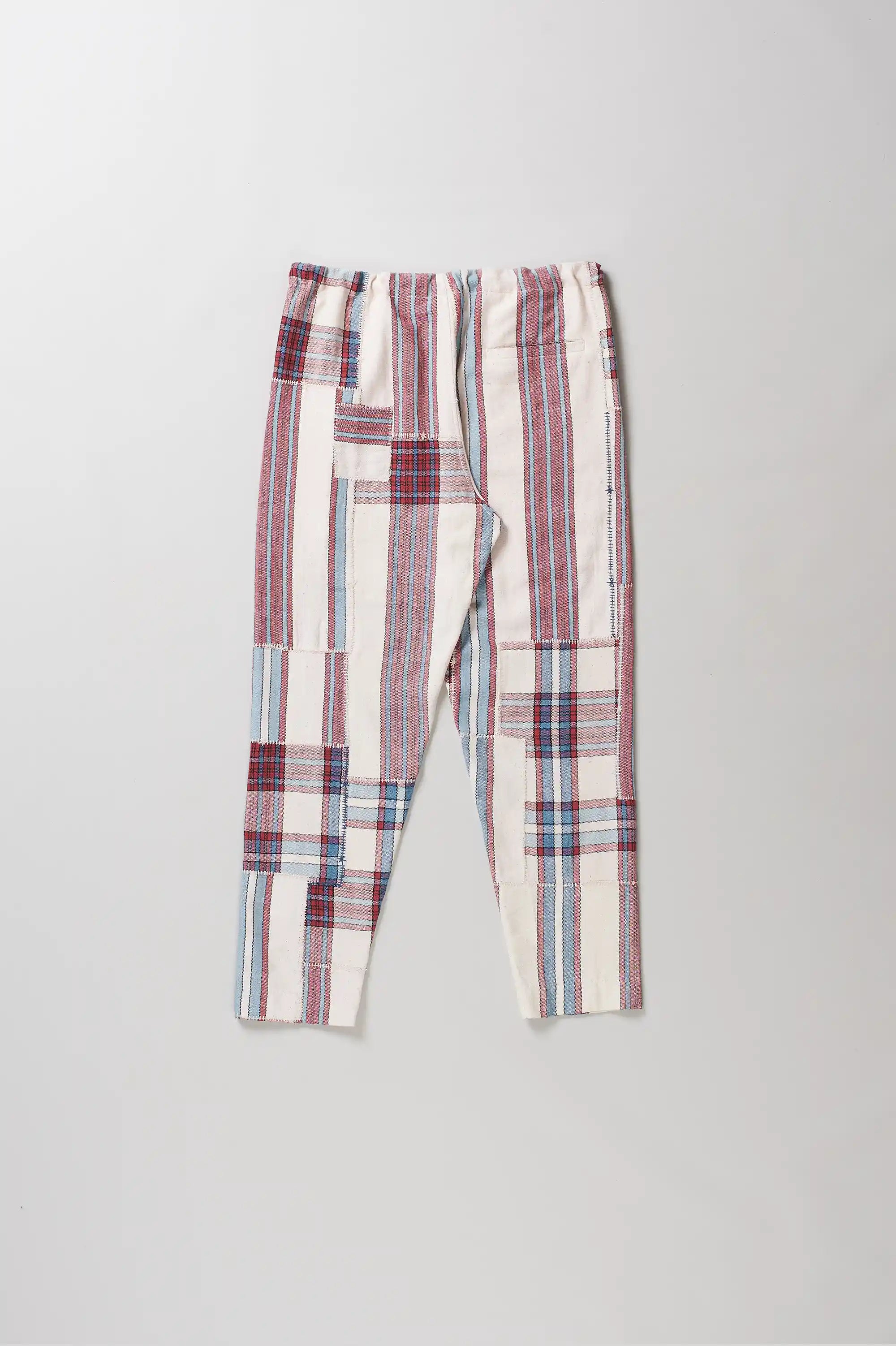 A pair of patchwork pants in pink, red, blue, and white, featuring a drawstring waistband, laid flat against a light grey background.