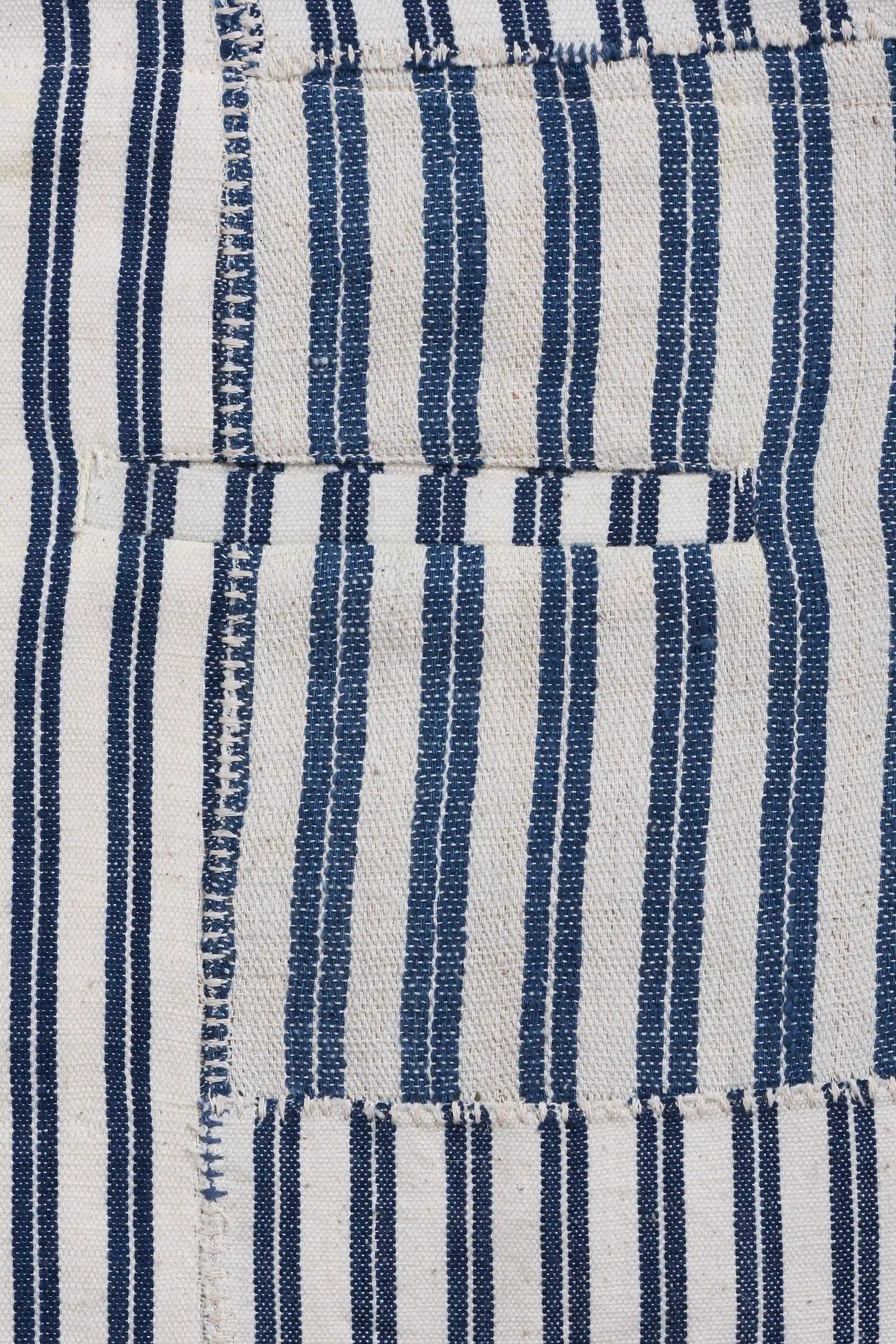 Close-up of a striped woven textile with vertical indigo and off-white stripes and visible stitching.