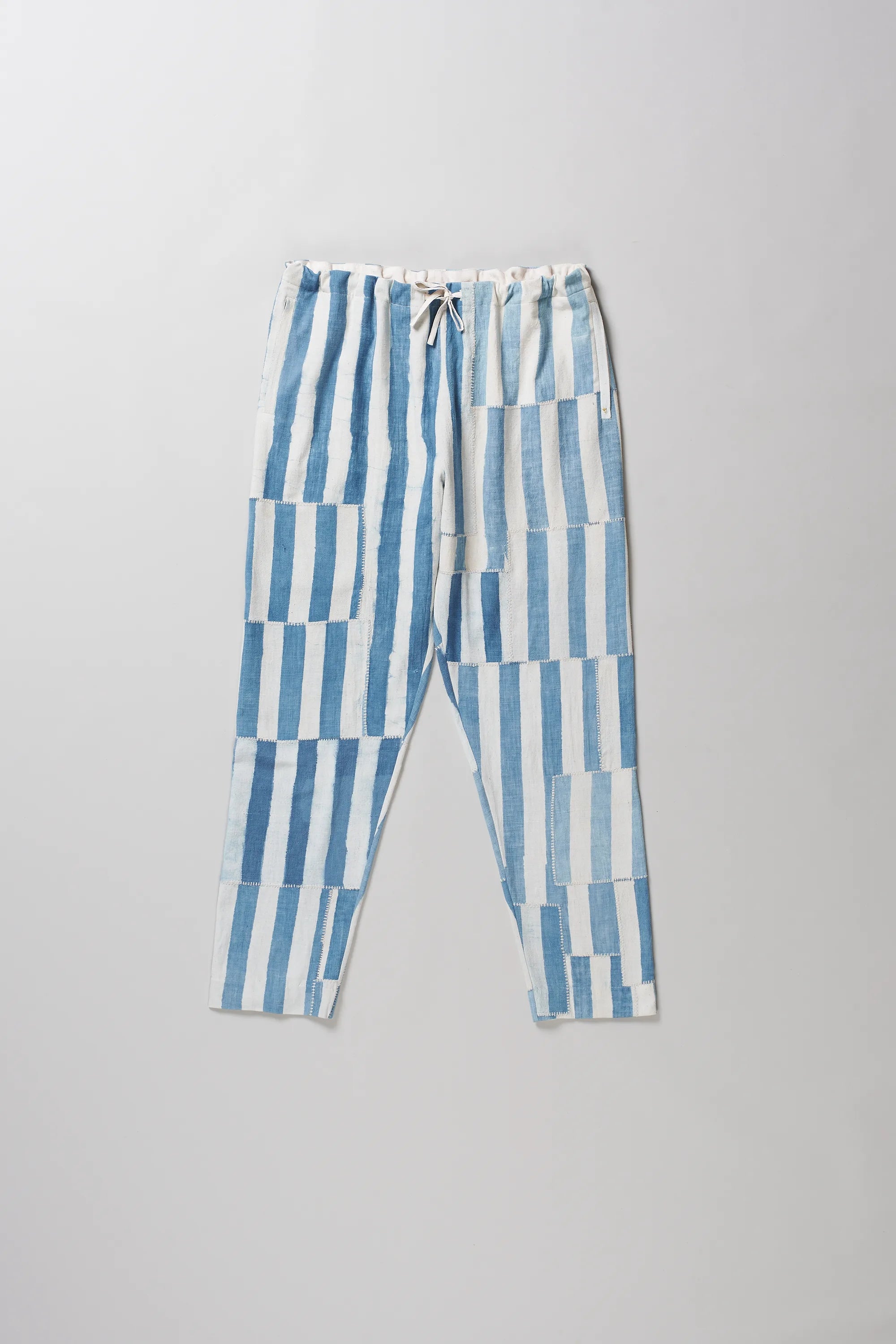 Light indigo and white vertically striped cropped pants with a drawstring waist, laid flat on a light grey background.