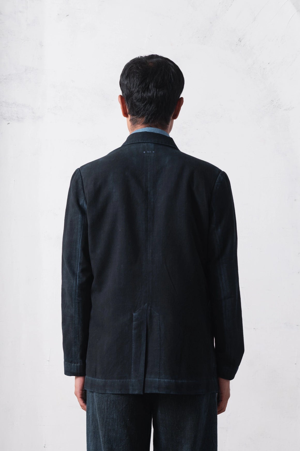 Back shot of a person wearing a black jacket and pants against a light grey background